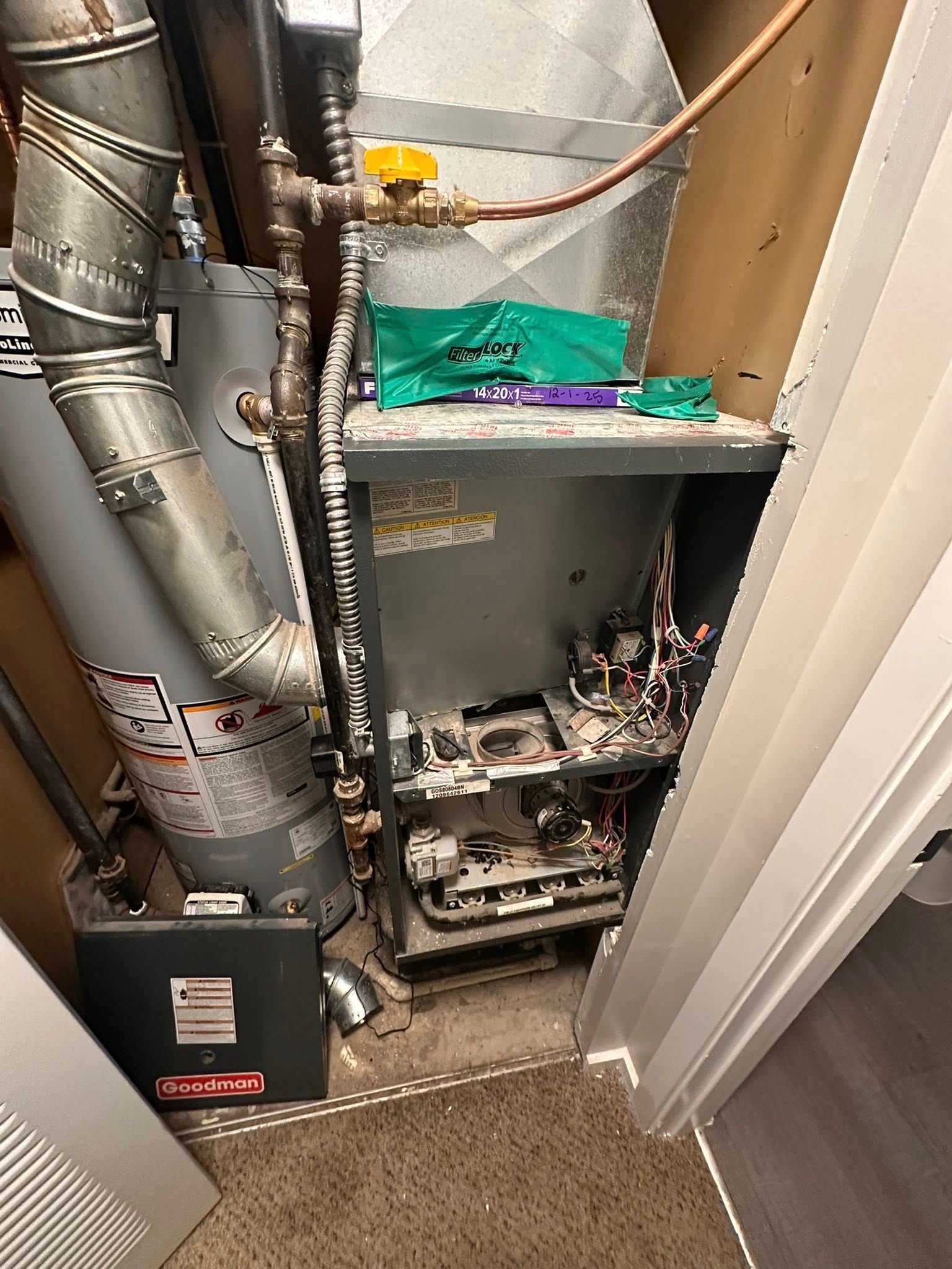 An open furnace and a water heater installed in a utility closet with exposed plumbing and a detached metal panel.