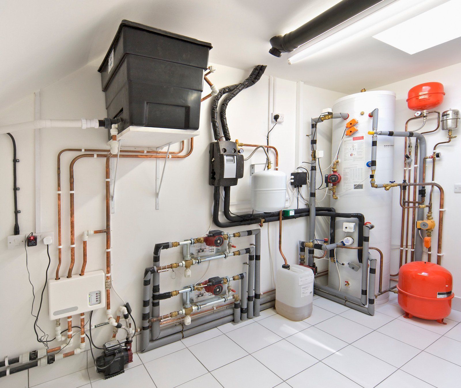 A utility room featuring a complex HVAC system with copper pipes, a white water tank, and orange expansion vessels.
