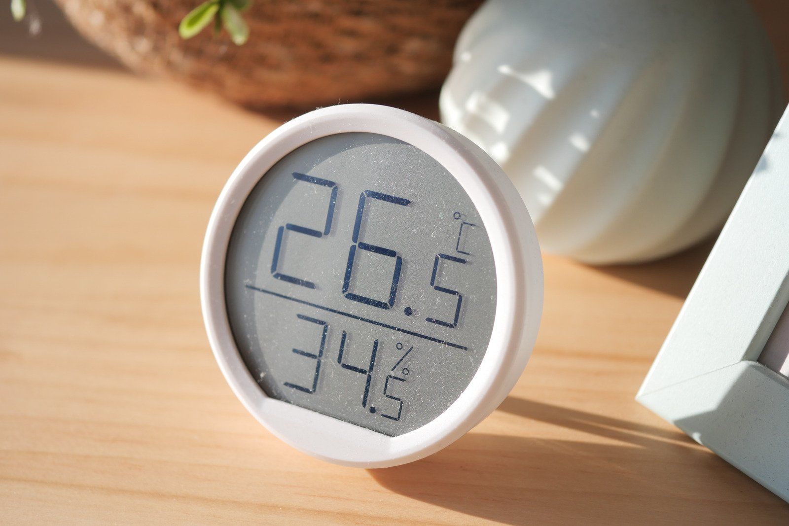 A small, round white digital thermometer and hygrometer showing 26.5°C and 34.5% humidity, resting on a wooden surface.
