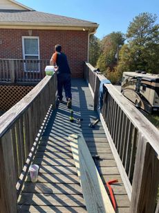 Person on a wooden ramp, with tools.  Ramp leads to a house; RV parked nearby. Sunny day.