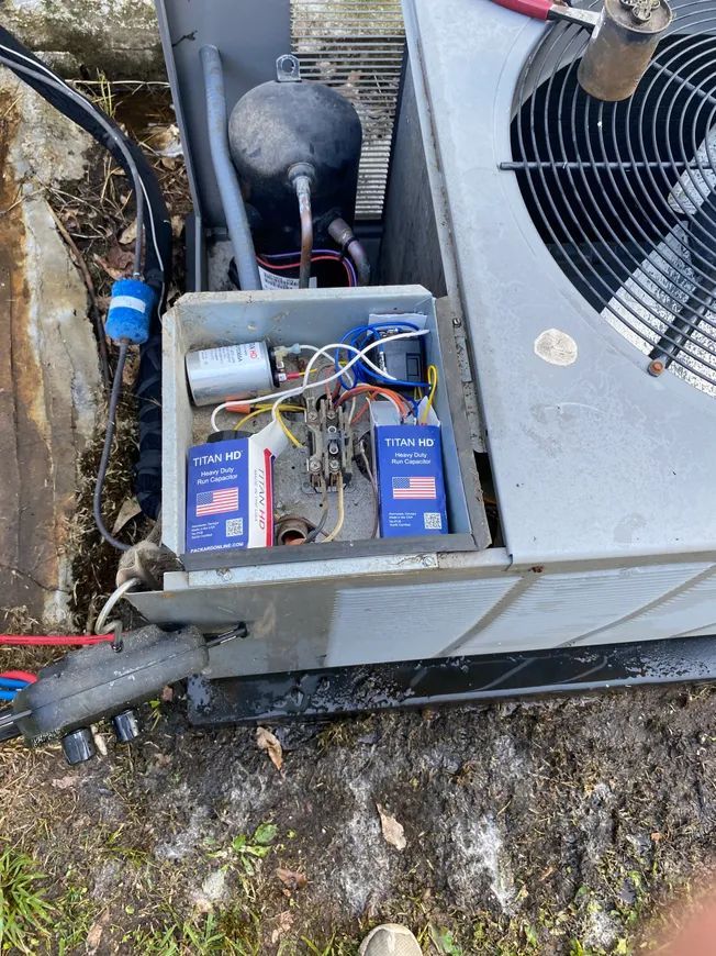 Air conditioning unit with open electrical panel showing capacitors and wiring.