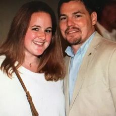 Woman with brown hair and white shirt smiles next to a man in a tan jacket.