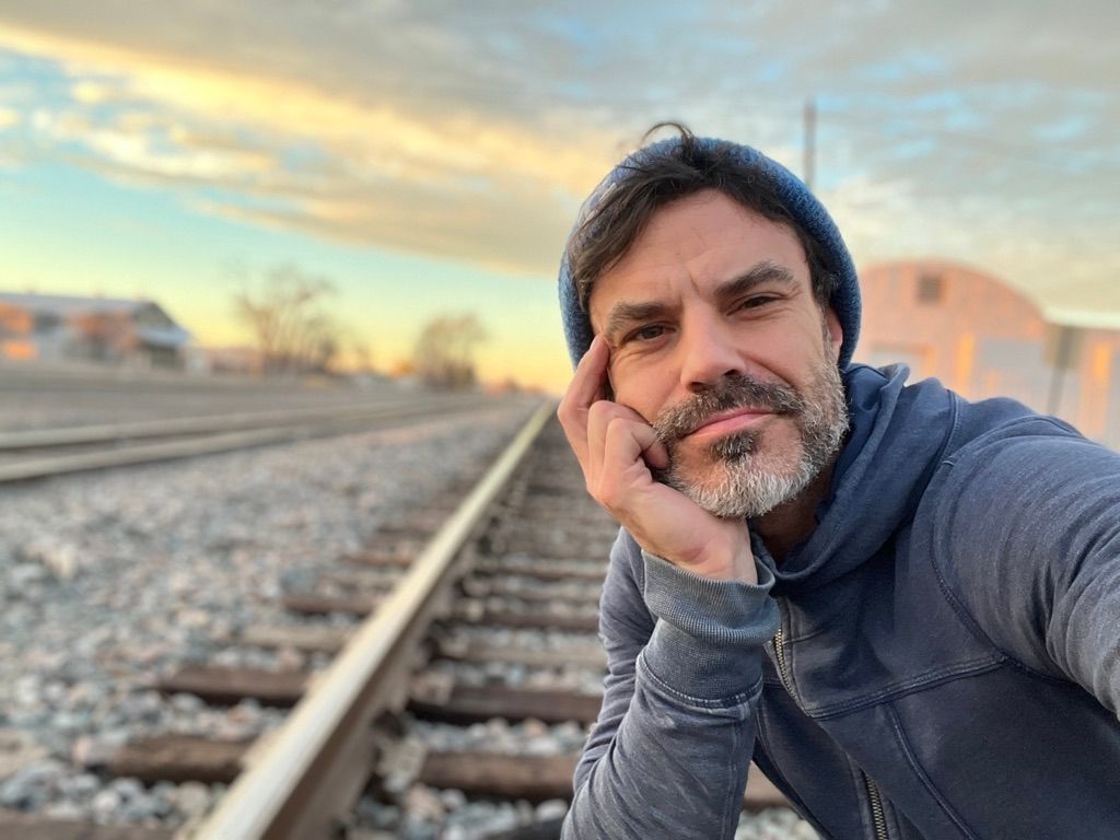 A man with a beard is taking a selfie on train tracks.