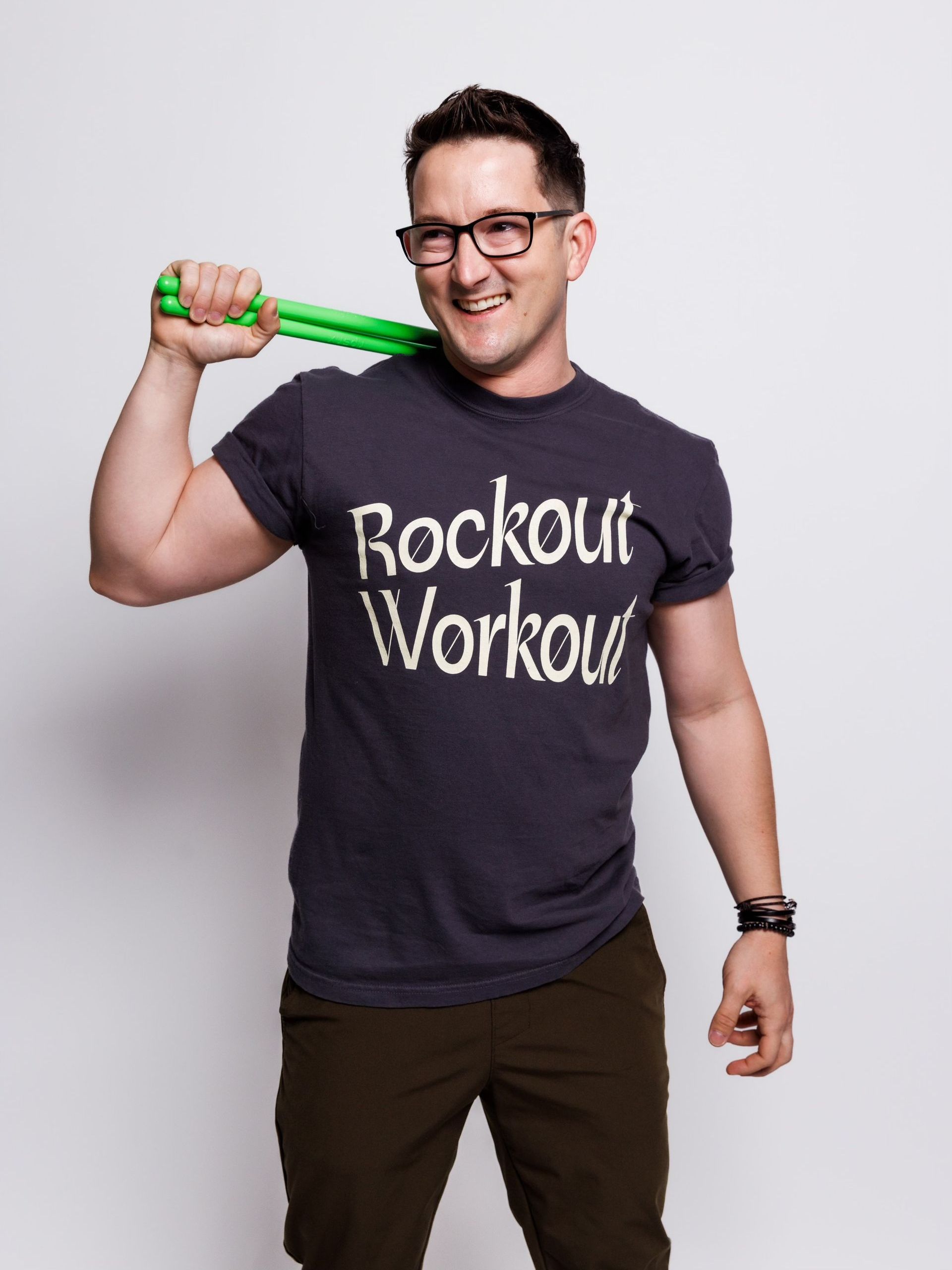A man wearing a rockout workout shirt is holding a green resistance band