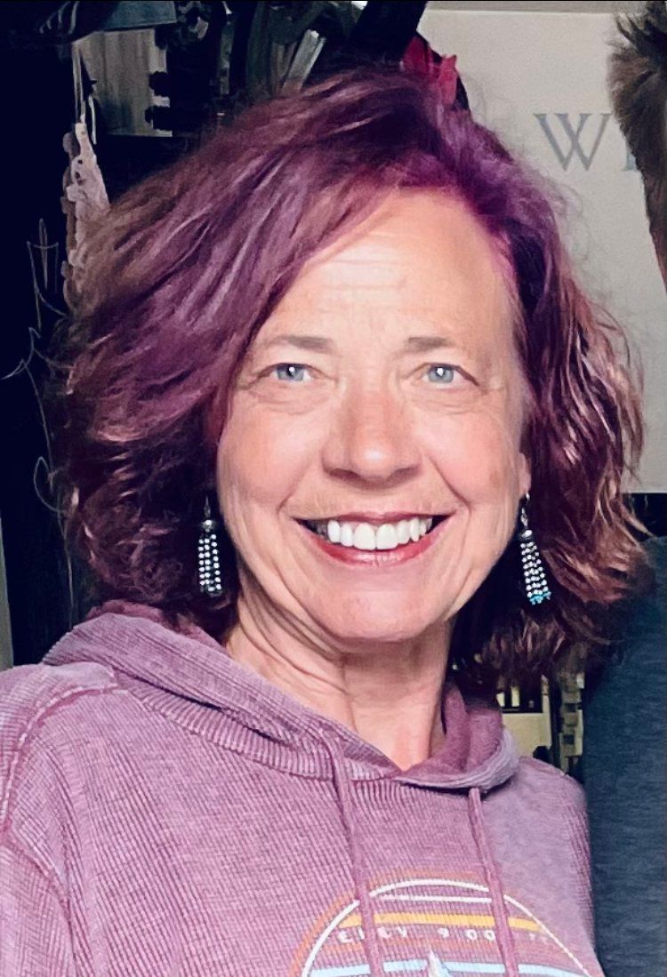 A woman with purple hair is wearing a purple hoodie and smiling.