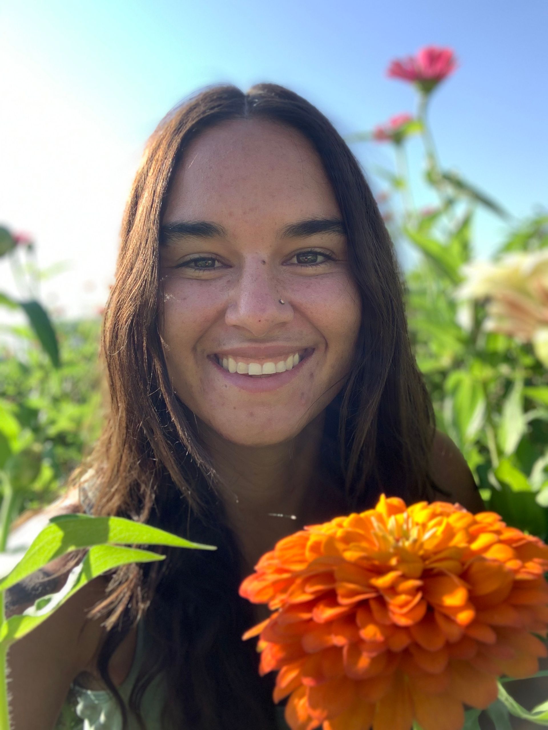A woman is smiling while holding an orange flower