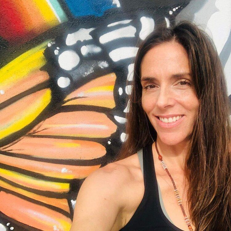 A woman is smiling in front of a painting of a butterfly wing.