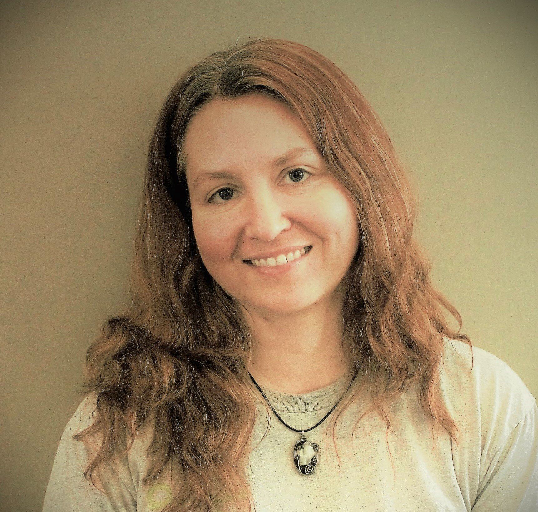 A woman with long red hair is smiling and wearing a necklace