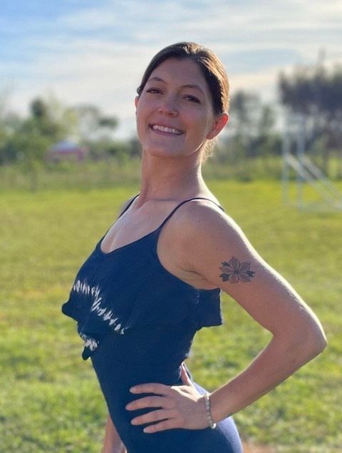 A woman with a tattoo on her arm is standing in a field