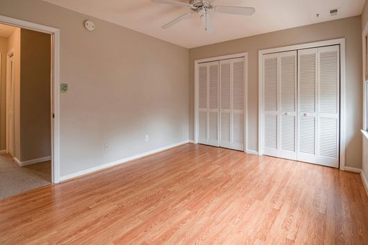 Empty room with light wood floors, neutral walls, two white closet doors, and a ceiling fan.