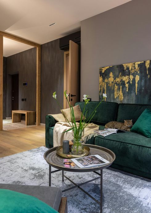 Emerald green sofa in modern living room with cat, art, and round coffee table.