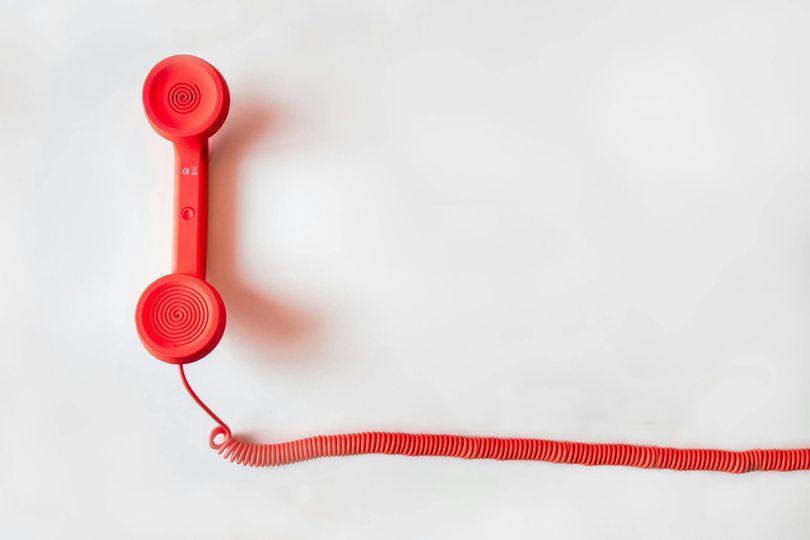 Red telephone receiver with coiled cord against a white background.