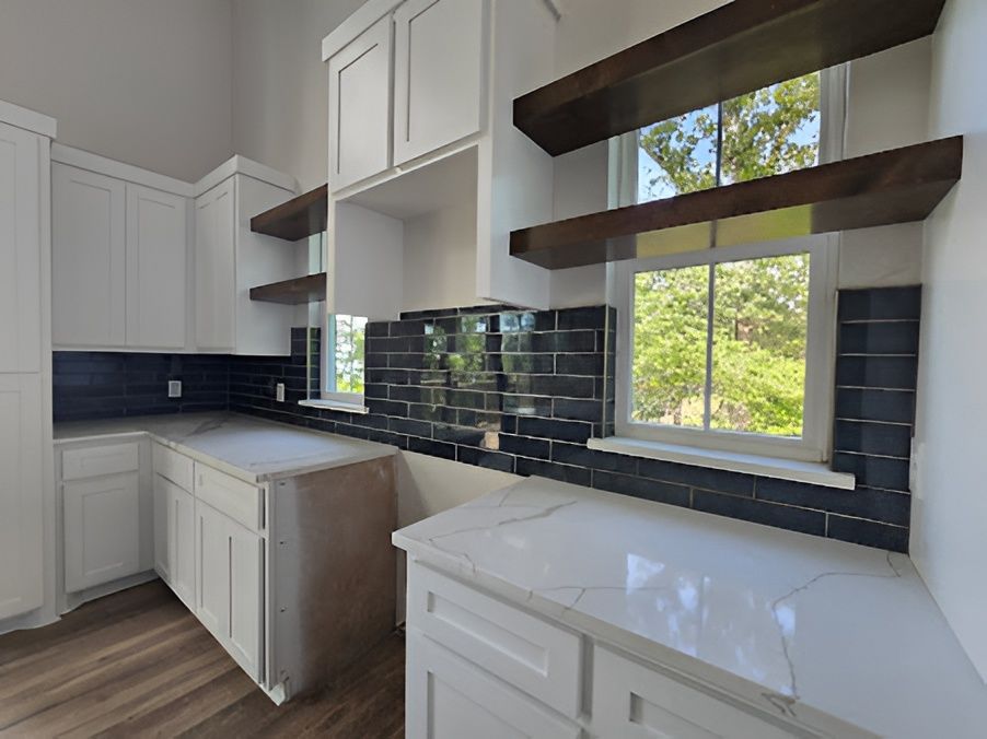 White kitchen with dark blue tile backsplash, open shelves, and a window overlooking greenery.