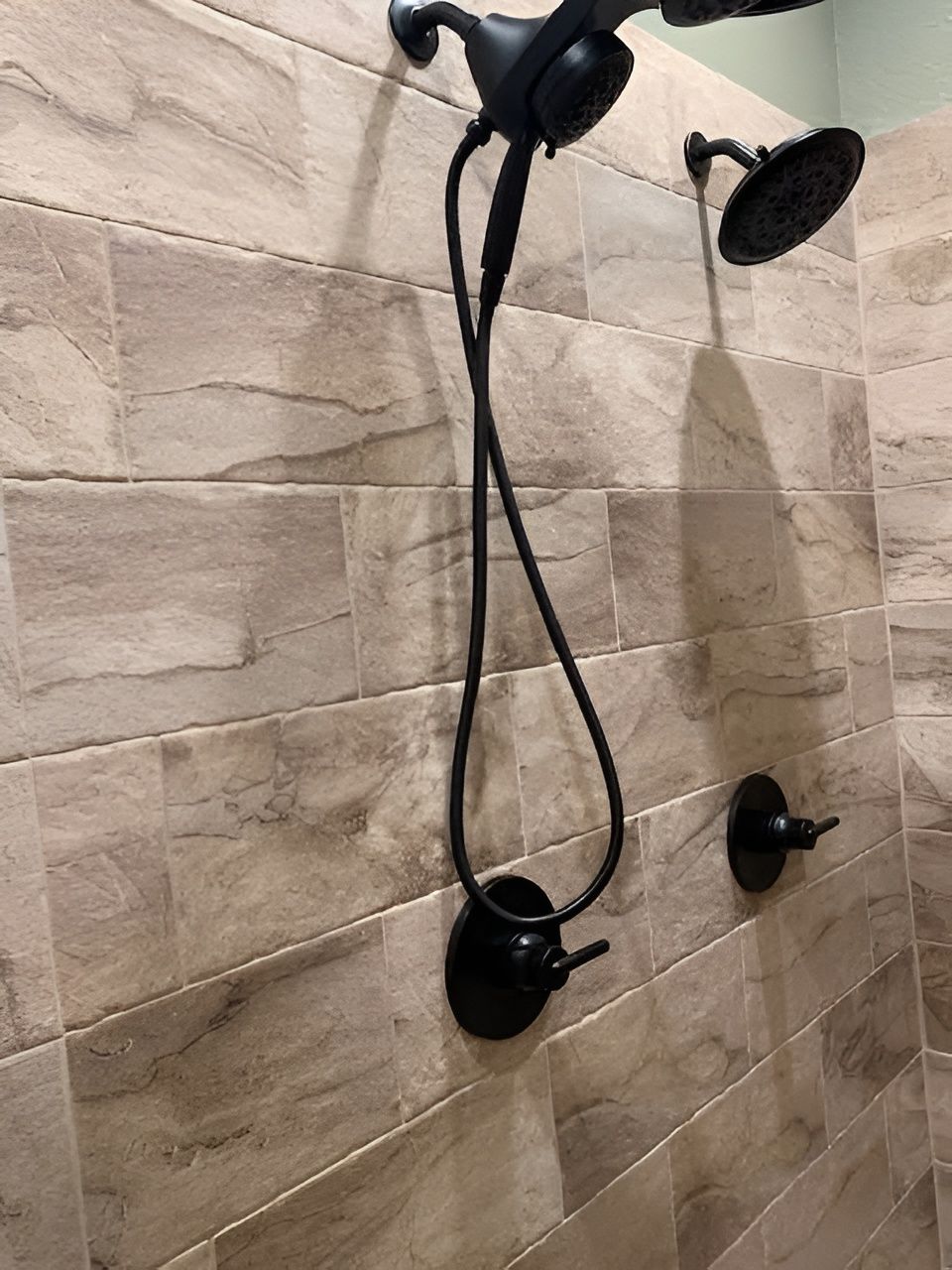 Black shower fixtures against beige tiled wall.