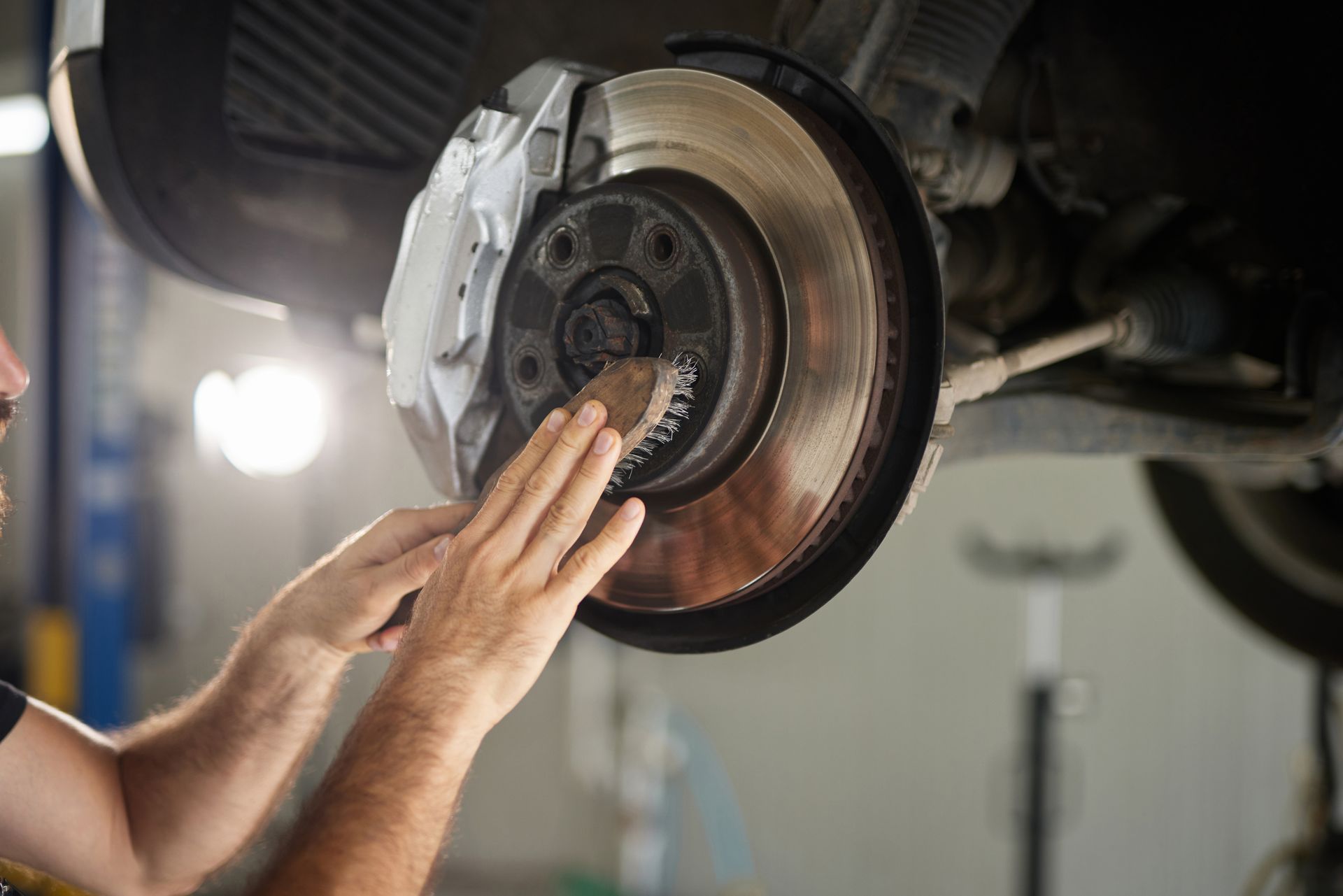 Mechanic working on car brake system, rotor and caliper visible in garage.