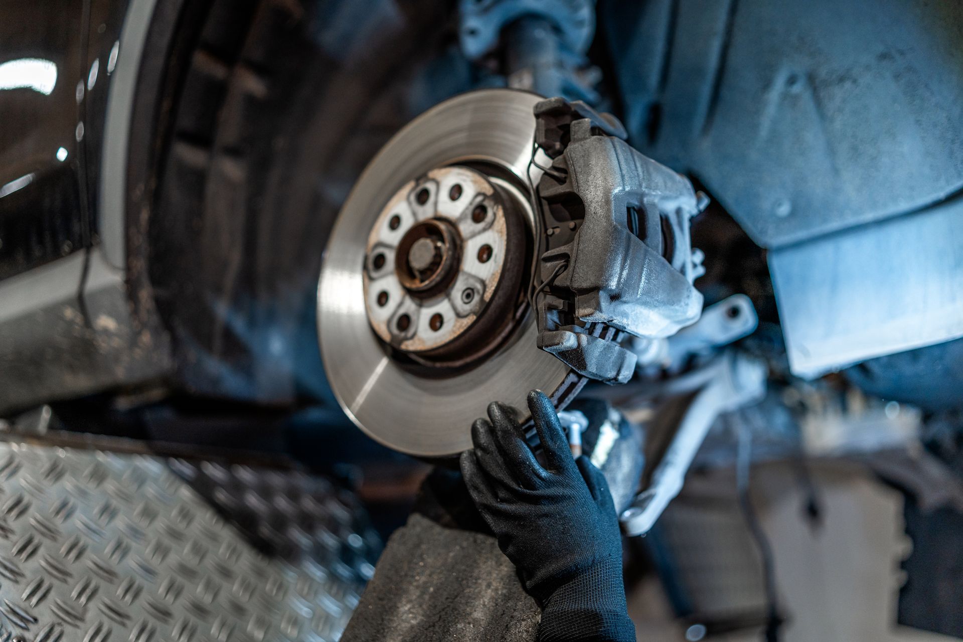 Mechanic replacing a car brake rotor with a gloved hand in a garage