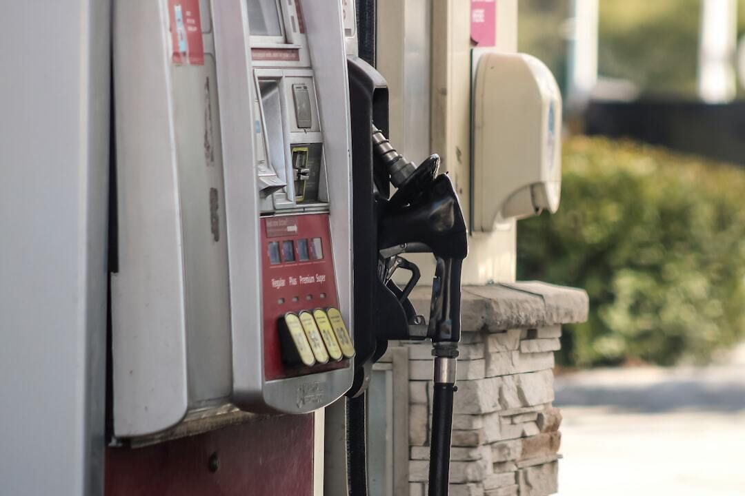 A woman is standing next to a motorcycle at a gas station.