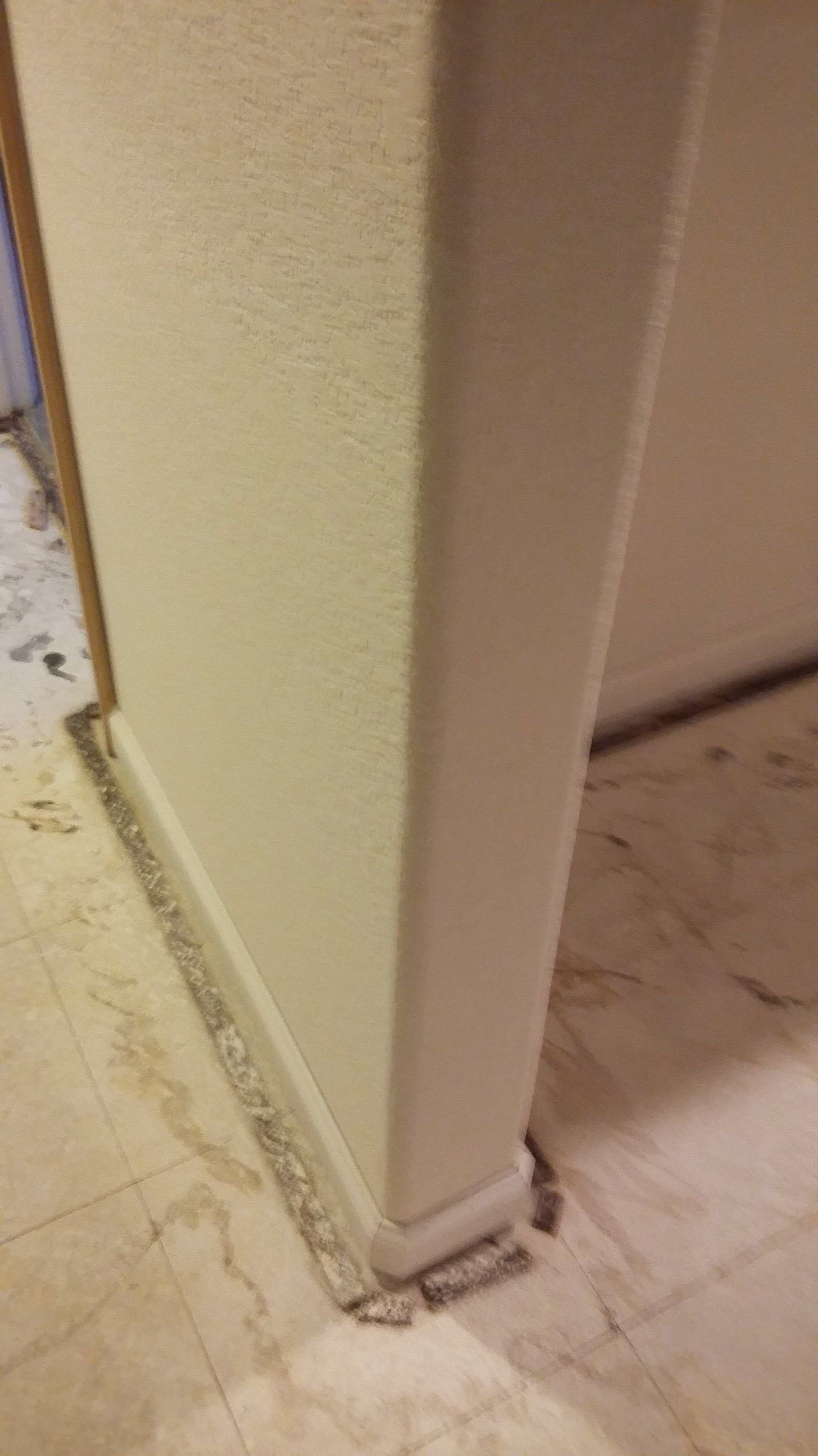 A corner of a room with a white wall and a marble floor.