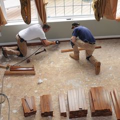 Two men are working on a wooden floor in a room