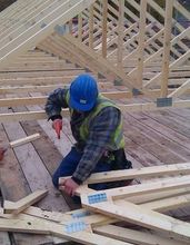 A man in a blue hard hat is working on a wooden structure.