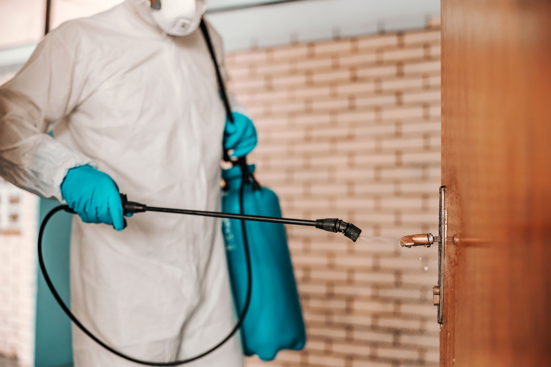 A man in a protective suit is spraying a door with a sprayer.