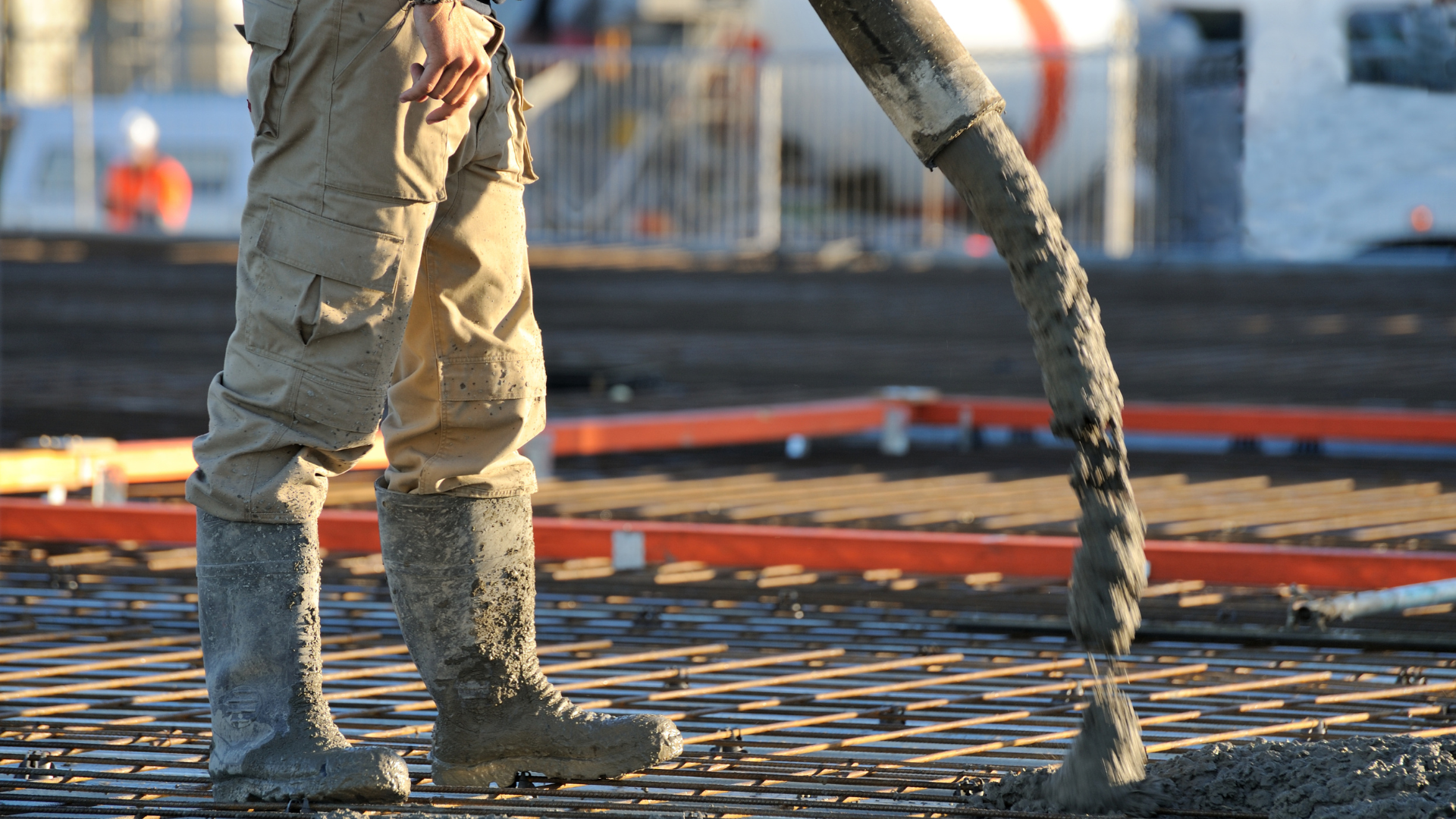 Construction worker pouring concrete onto a rebar grid at a construction site.