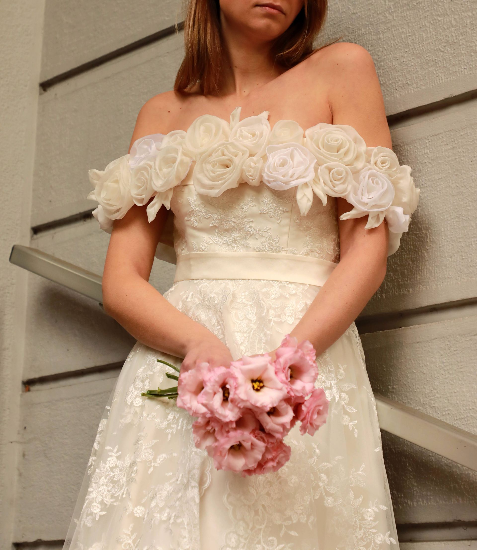 Una donna in abito bianco tiene in mano un mazzo di fiori rosa