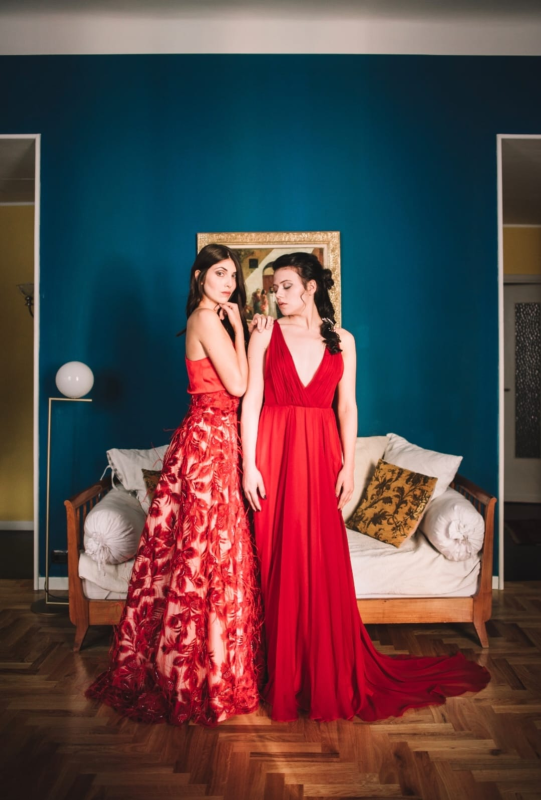 Due donne vestite di rosso sono in piedi una accanto all'altra in un soggiorno.