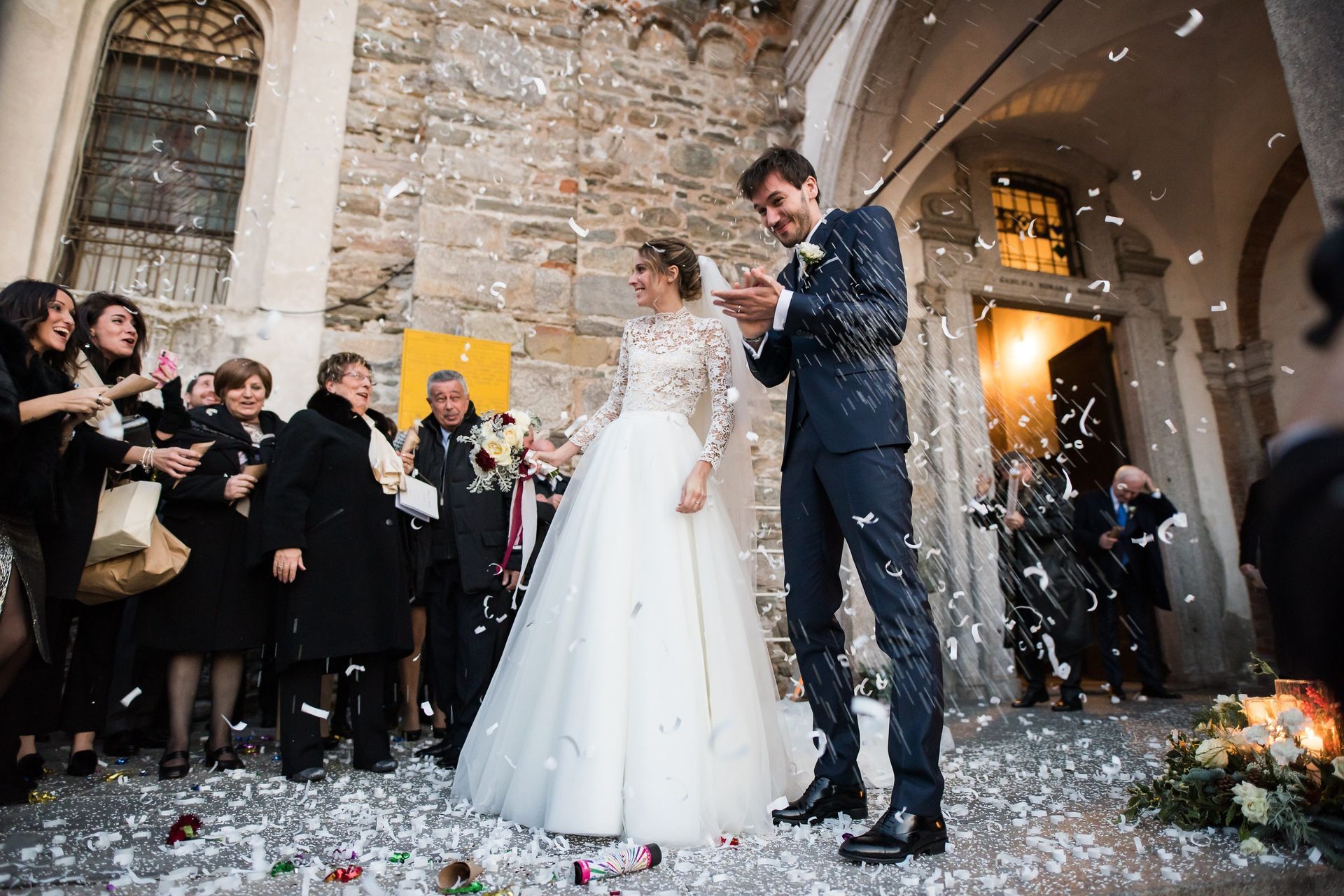 Una coppia di sposi sono in piedi davanti a una chiesa circondati da coriandoli.