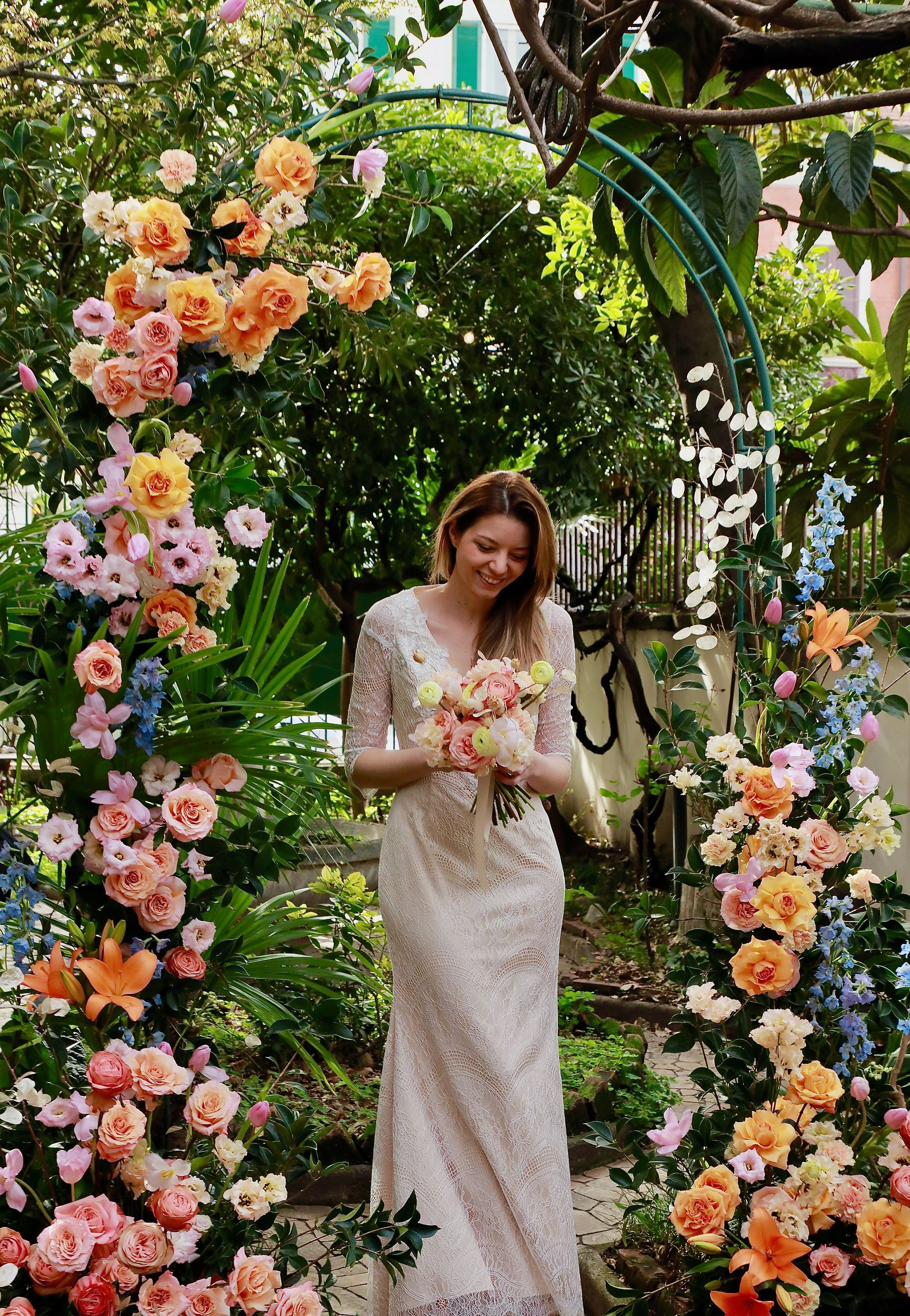 Una donna in abito da sposa è in piedi in un giardino con in mano un mazzo di fiori.