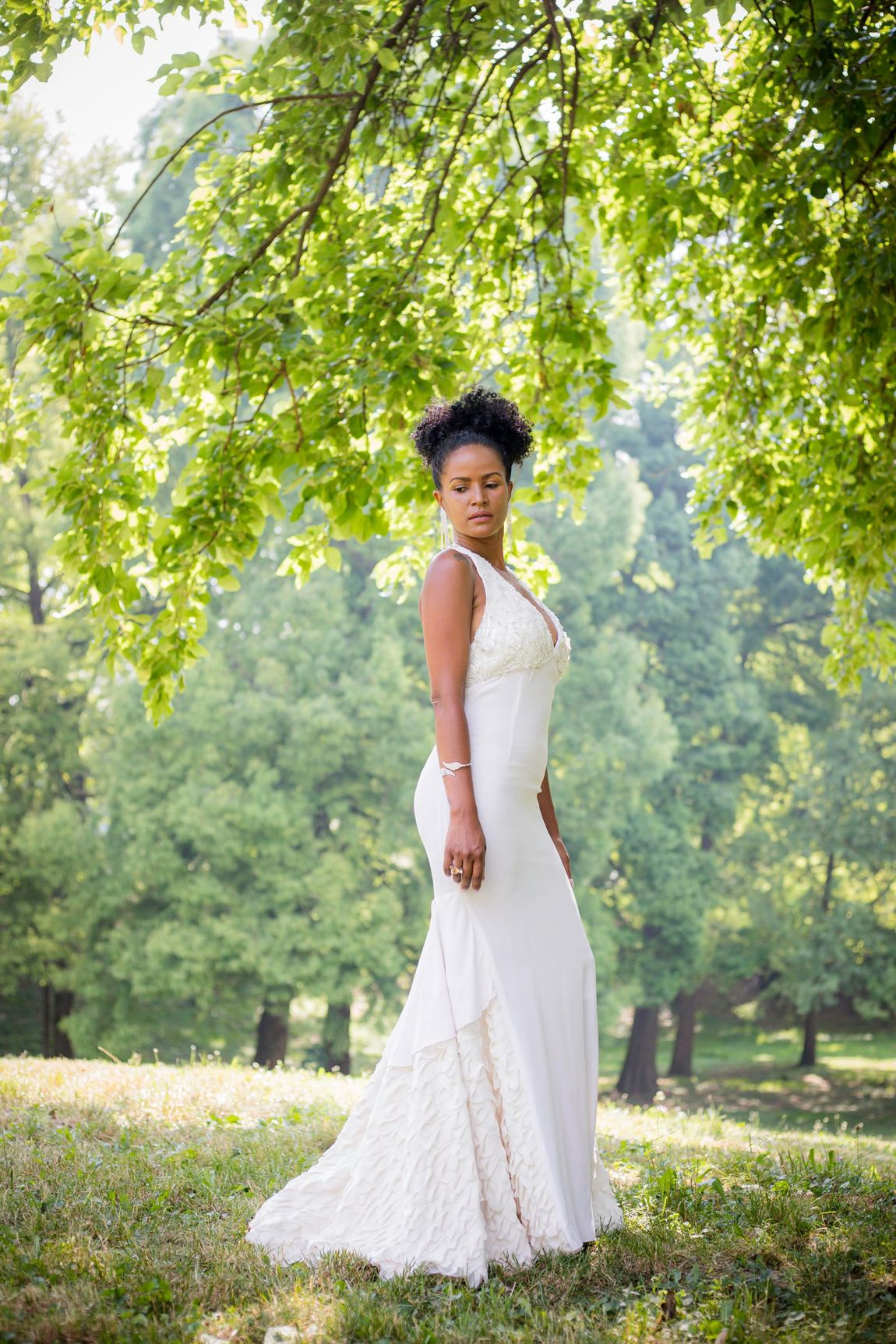 Una donna con un abito da sposa bianco è in piedi sotto un albero in un parco.