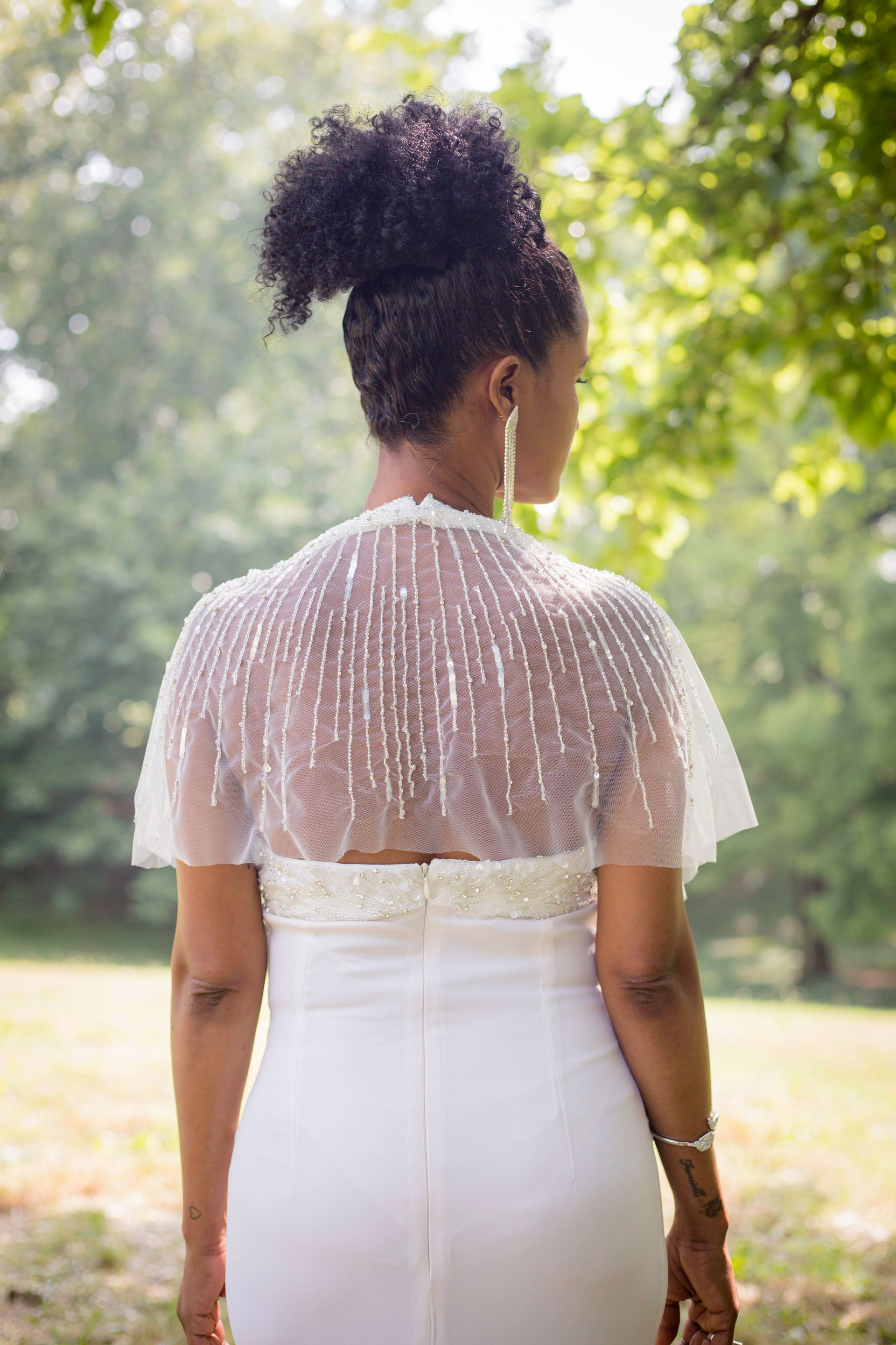 La schiena di una donna che indossa un abito bianco e un mantello bianco.