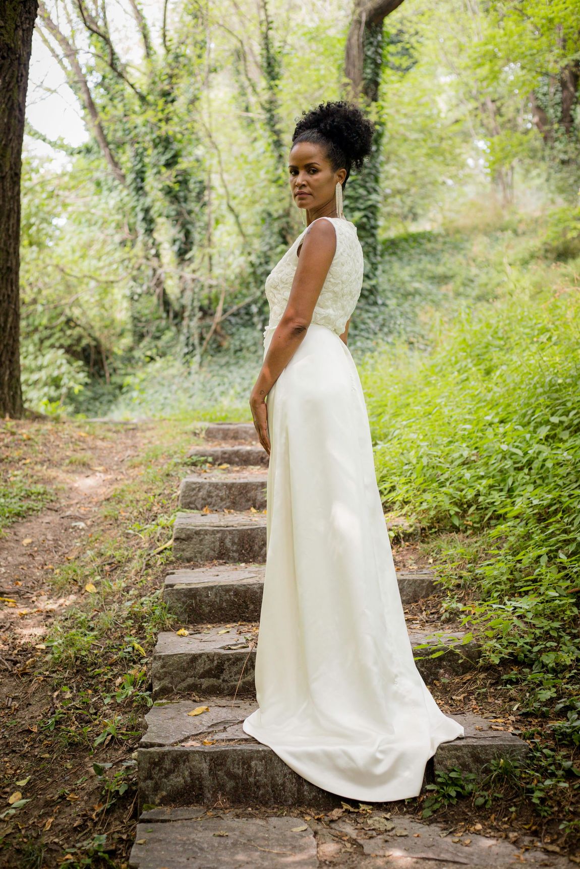Una donna in abito da sposa è in piedi sulle scale nel bosco.