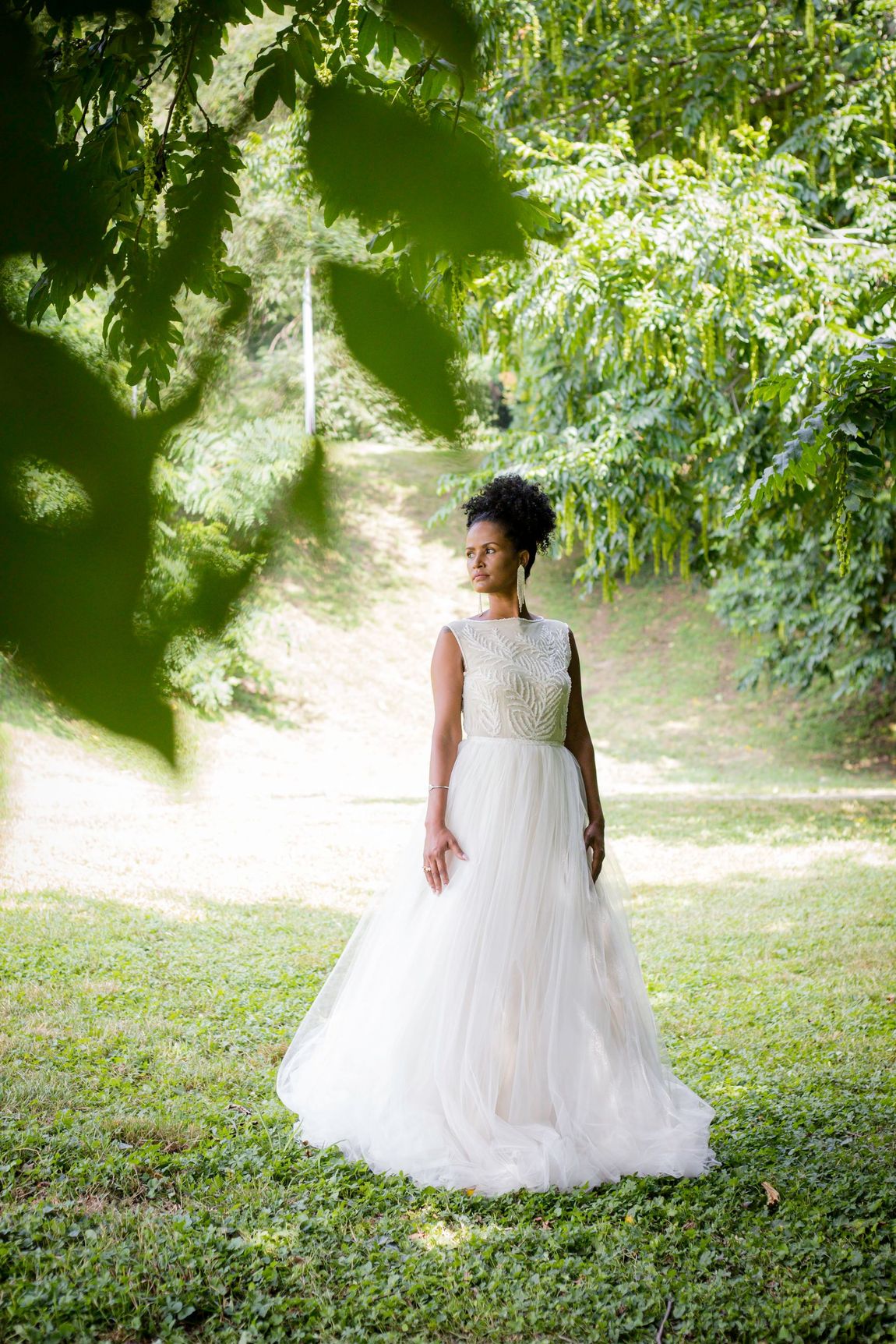 Una donna in abito da sposa è in piedi sull'erba sotto un albero.