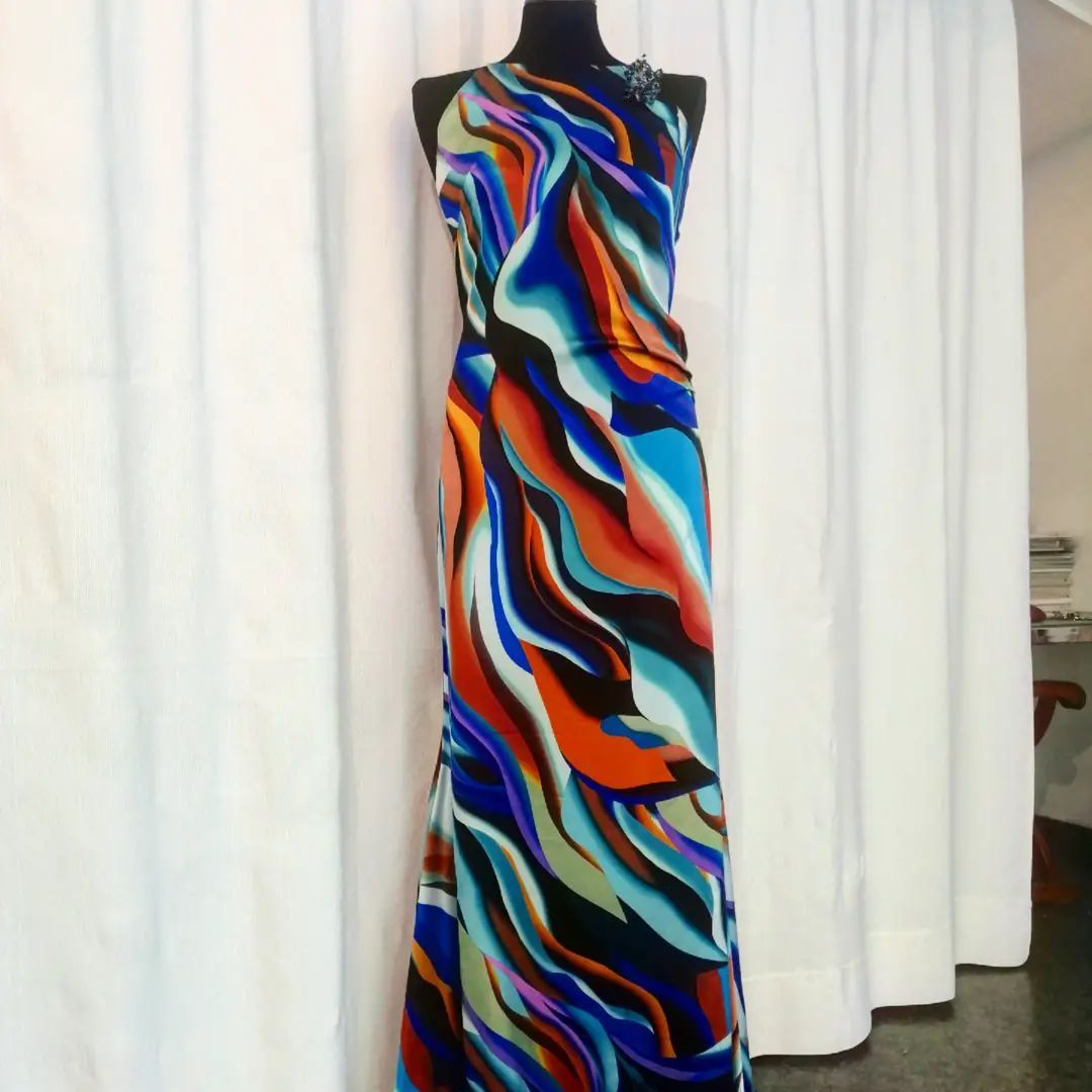 Un vestito colorato è su un manichino davanti a tende bianche