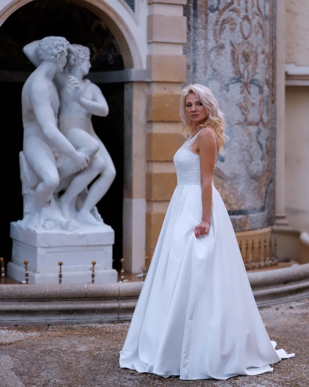 Una donna vestita di bianco è in piedi davanti a una statua.