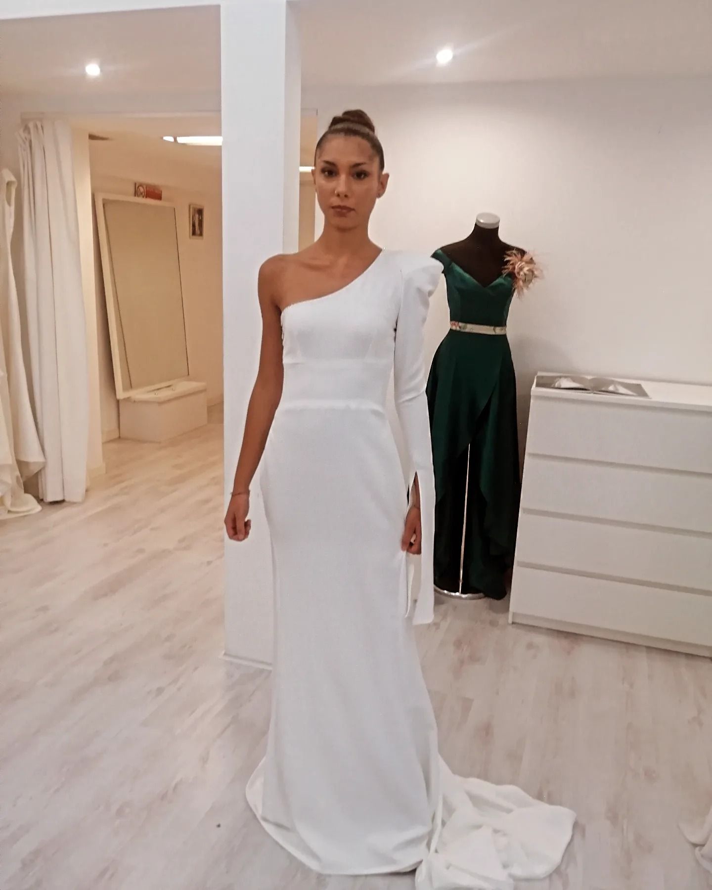 Una donna con un abito bianco monospalla è in piedi in una stanza