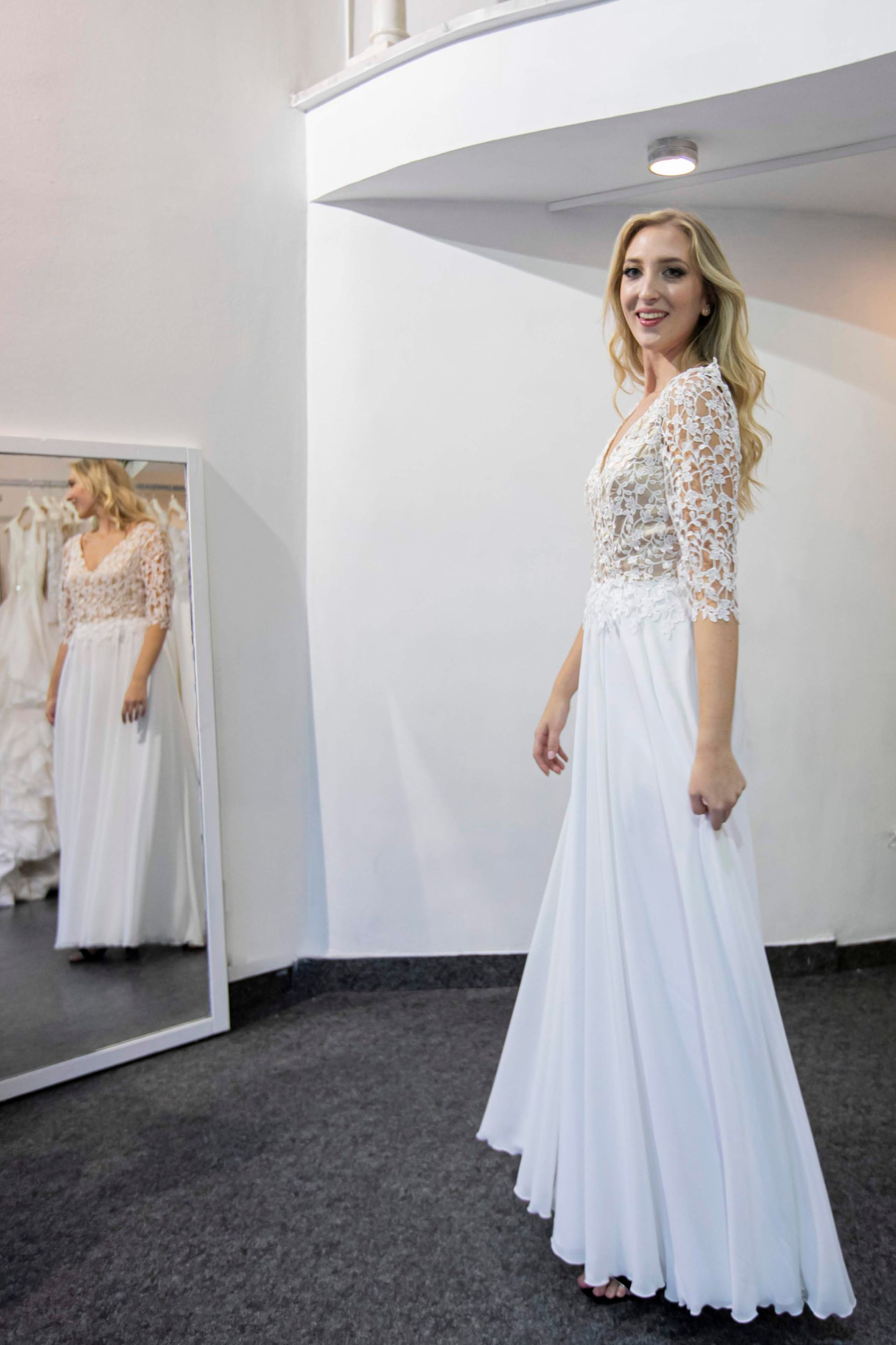 Una donna in abito da sposa bianco è in piedi davanti a uno specchio.