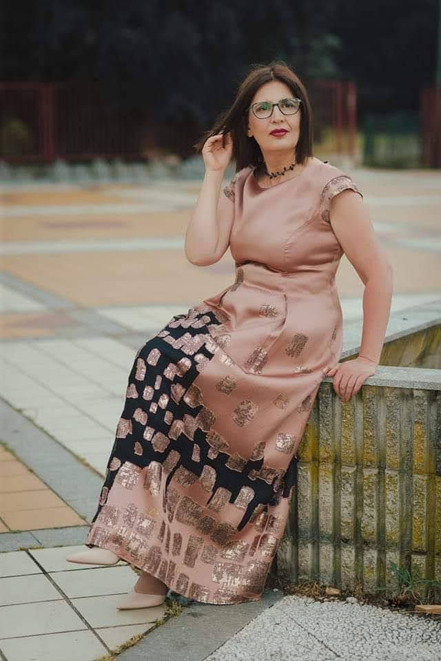 Una donna con un lungo abito e gli occhiali è seduta su un muro.