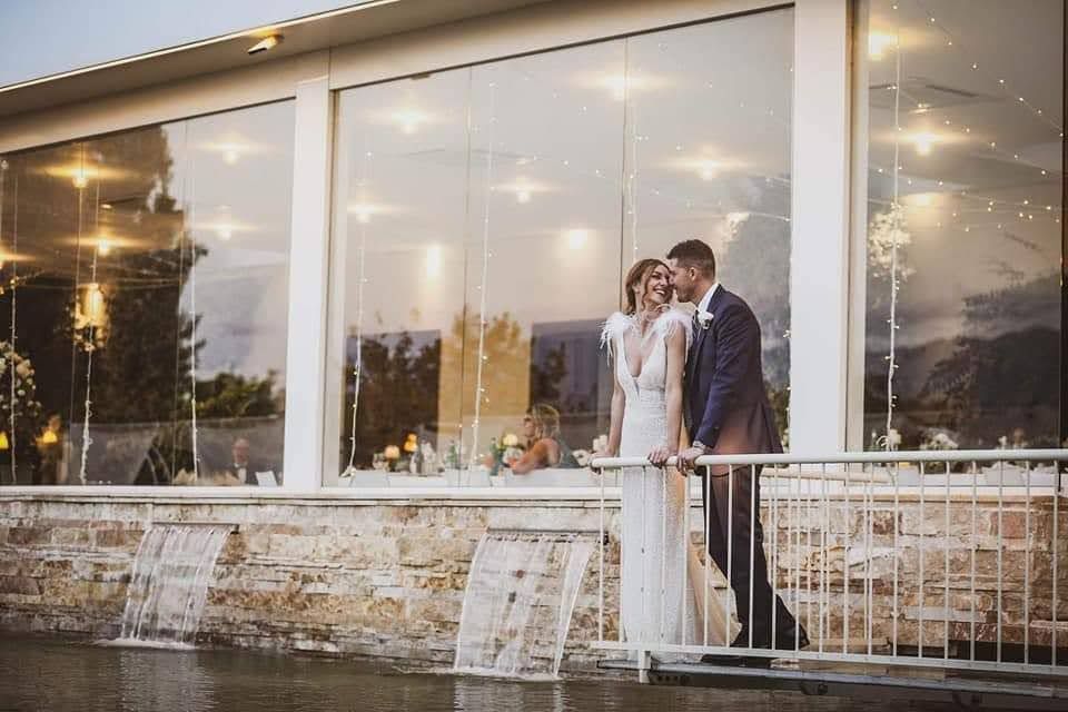 Una sposa e uno sposo si baciano davanti a una grande finestra.