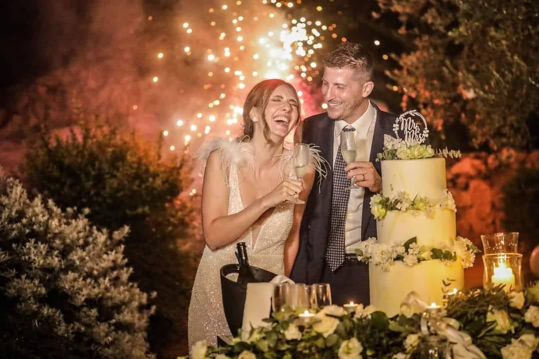 Una sposa e uno sposo tagliano la torta nuziale con fuochi d'artificio sullo sfondo.