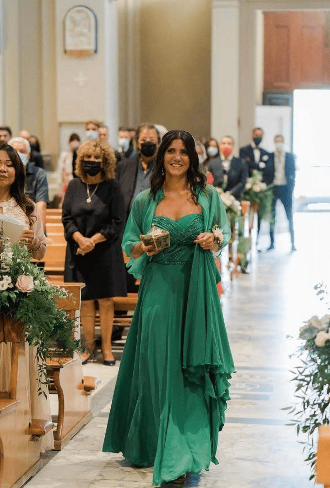 Una donna con un vestito verde sta camminando lungo la navata di una chiesa.