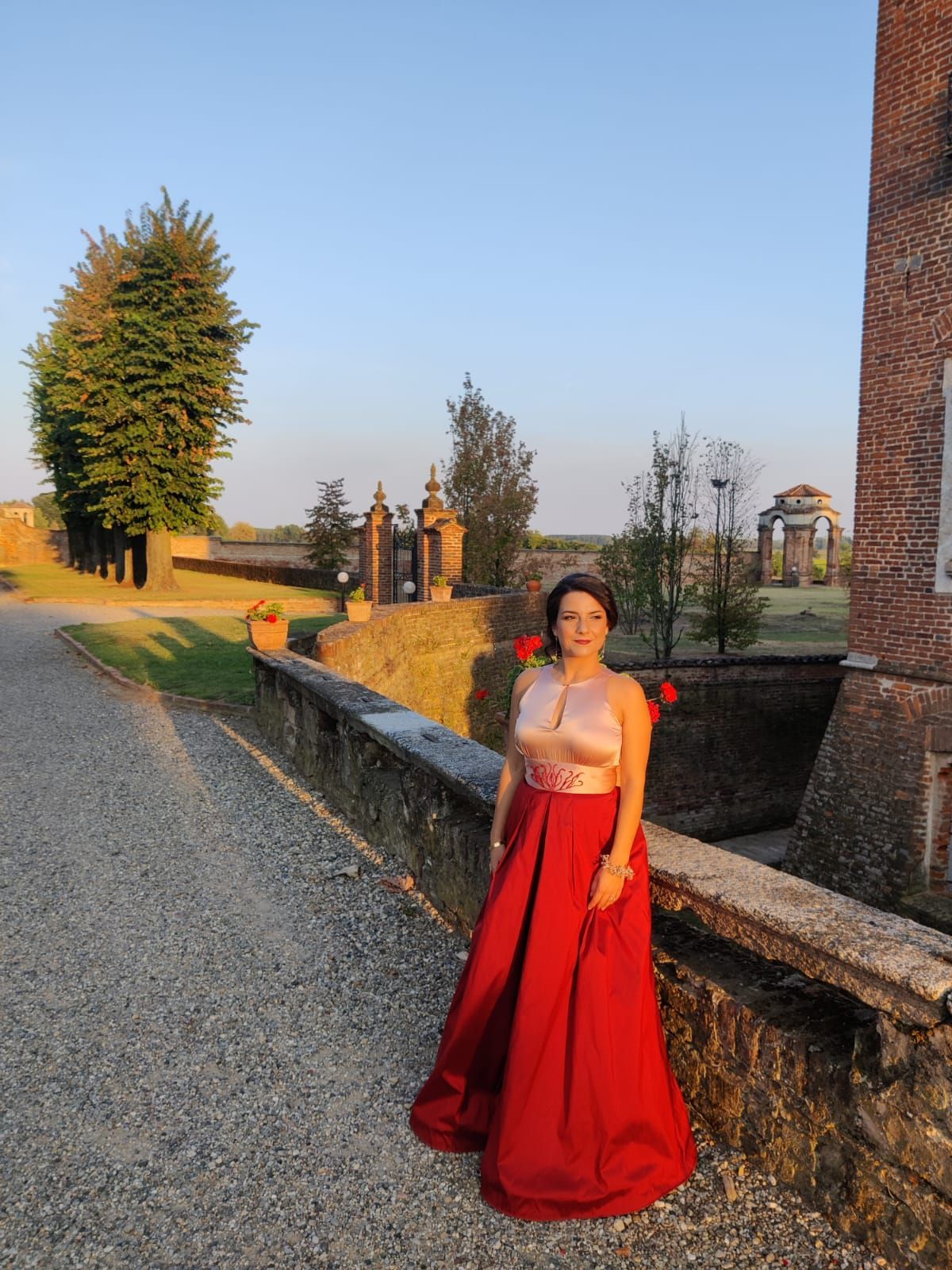 Una donna con un vestito rosso è in piedi accanto a un muro di pietra.