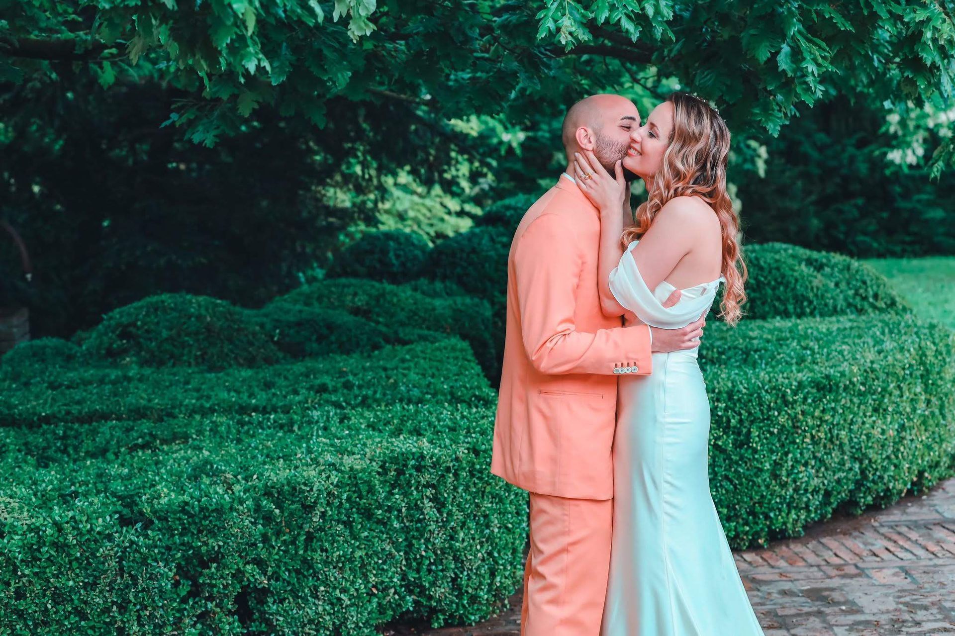 Una sposa e uno sposo si baciano davanti a una siepe.