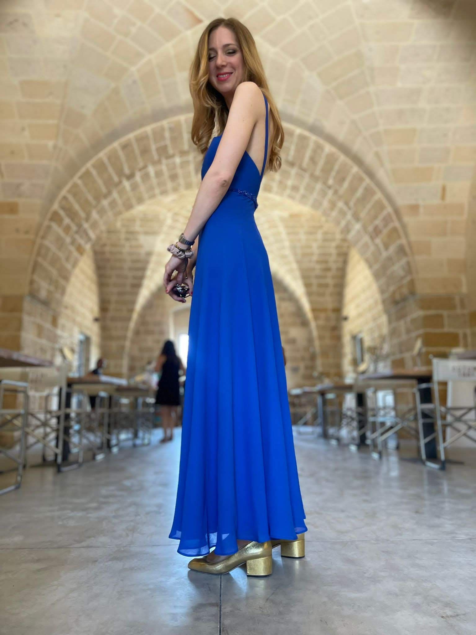 Una donna con un vestito blu è in piedi davanti a un arco di pietra.