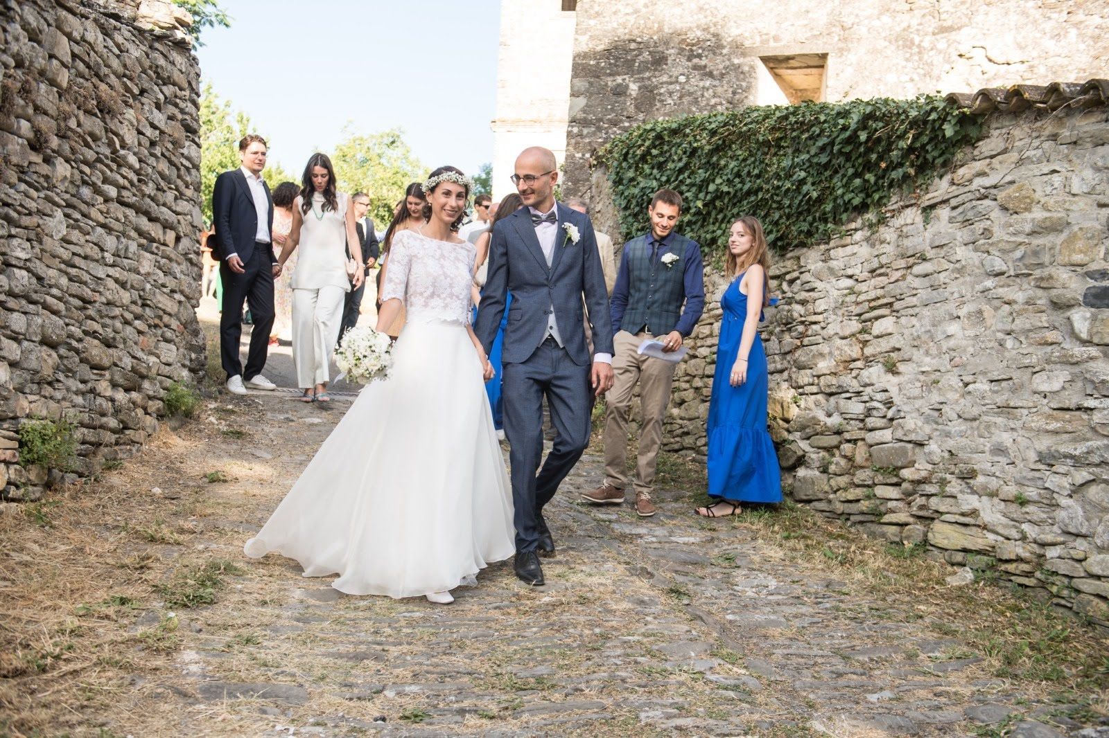 Una coppia di sposi sta camminando lungo una strada acciottolata con il loro corteo nuziale.