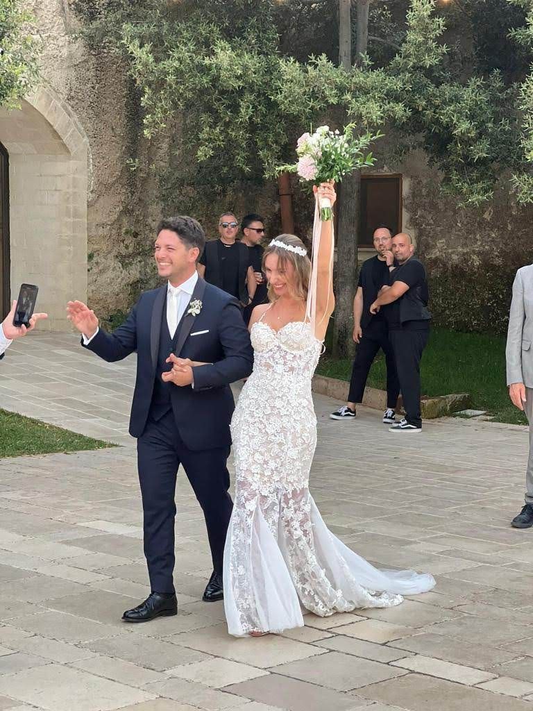 Una coppia di sposi cammina sul marciapiede con le braccia alzate.