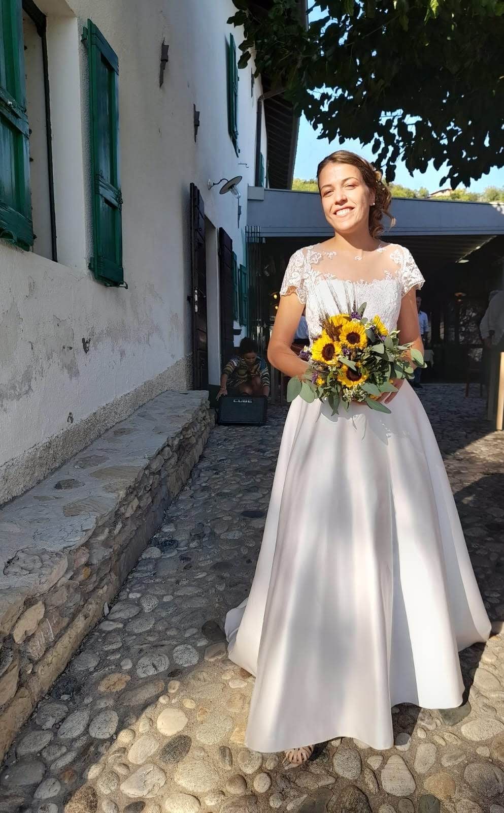 Una donna in abito da sposa tiene in mano un mazzo di girasoli.