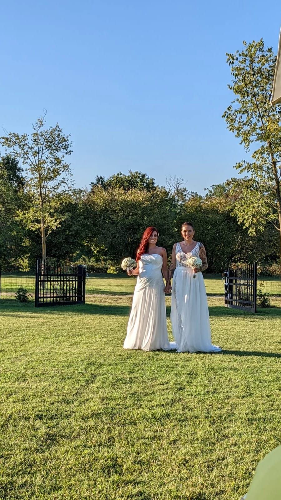 Due donne in abiti bianchi sono in piedi in un campo erboso.