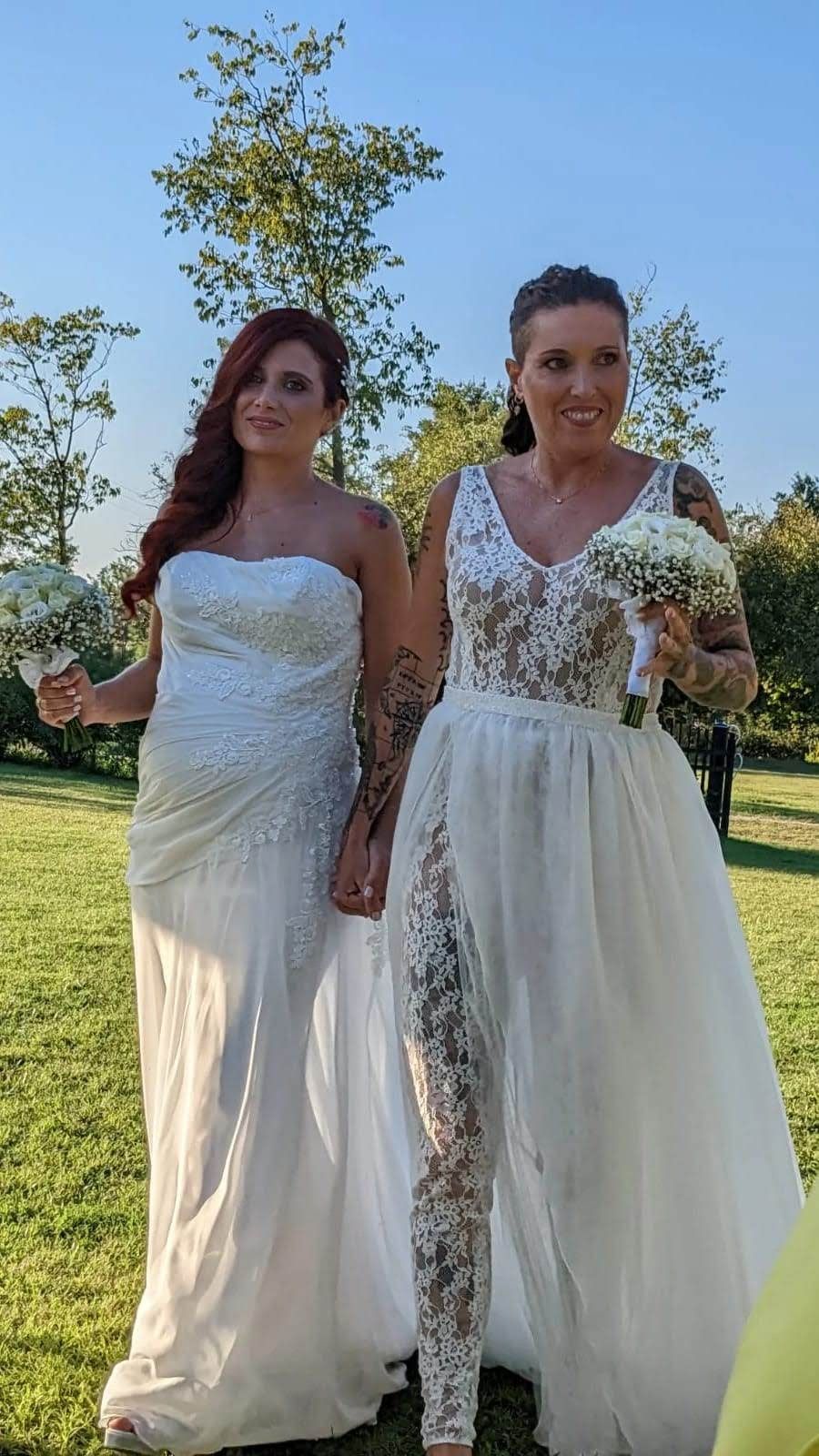 Due donne in abito da sposa sono in piedi una accanto all'altra in un campo.